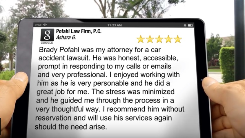 An image that shows a man holding an ipad with the google logo, wifi icon, time, battery icon, five golden stars, and the text " Brady Pofahl was my attorney for a car accident lawsuit. He was honest, accessible, promt in responding to my calls or emails and very professional. I enjoyed working with him as he is very personable and he did a great job for me. The stress was minimized and he guided me through the process in a very thoughtful way. I recommend him without reservation and will use his services again should the need arise. " on the screen with large trees on the in the background