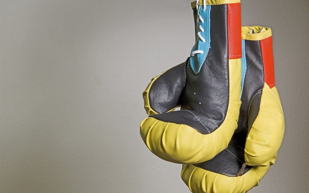 A pair of boxing gloves which represents the toughness of your motor vehicle attorney to fight the insurance company for your legal claims and with the colors of yellow, black, blue, and red that is hanged reversely by its white lace and having a plain gray background.